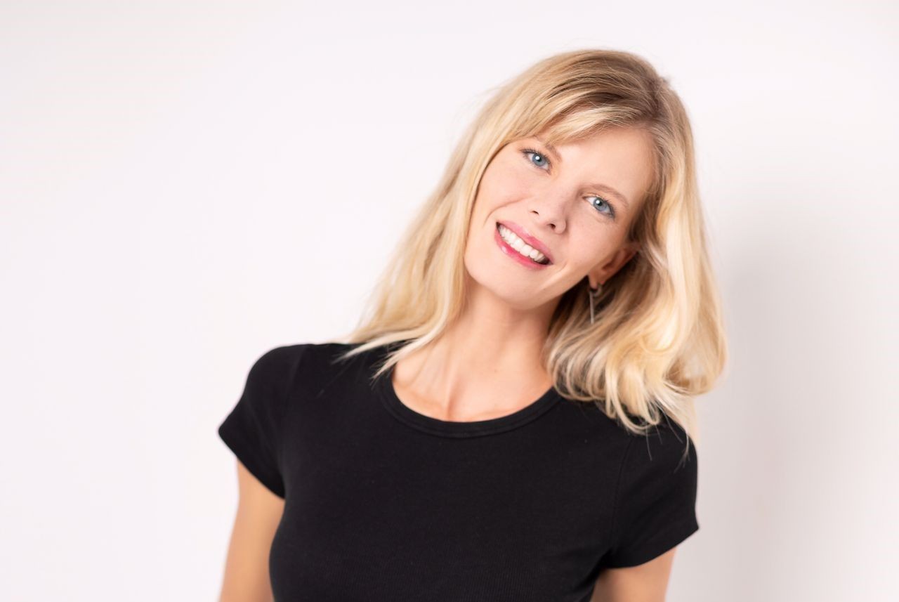 Person with shoulder-length blonde hair wearing a black t-shirt, against a plain white background.