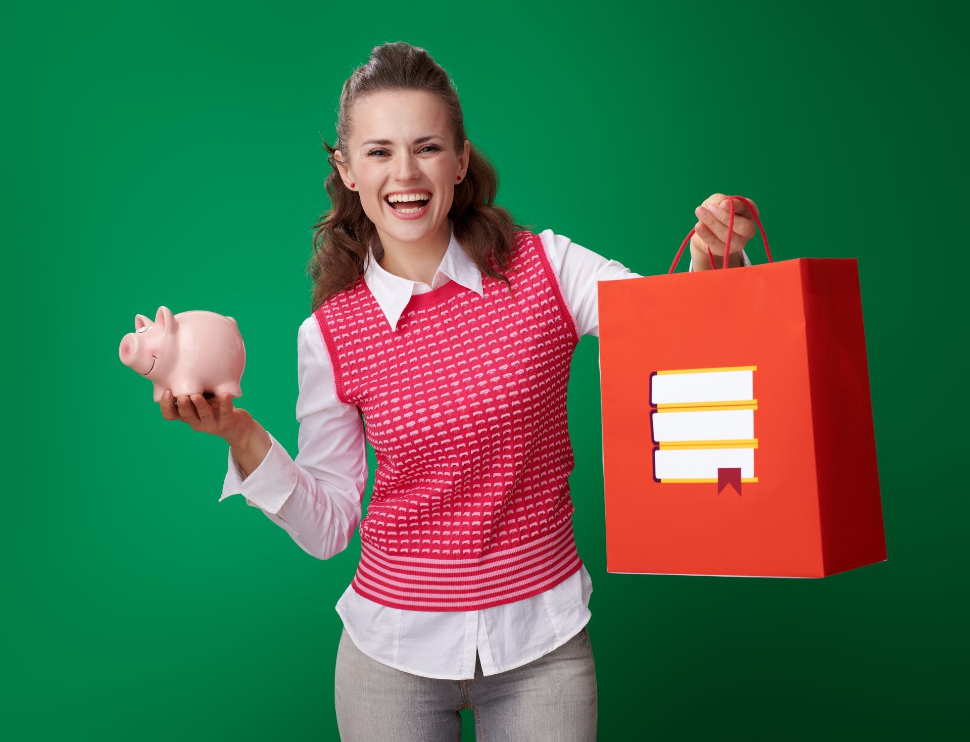 smiling modern student woman in a red waistcoat with shopping bag with books and piggy bank on green background