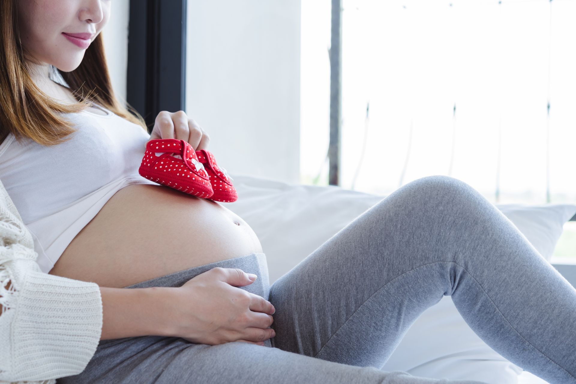Attractive pregnant woman holding a first baby shoes on her belly. Last months of pregnancy.
